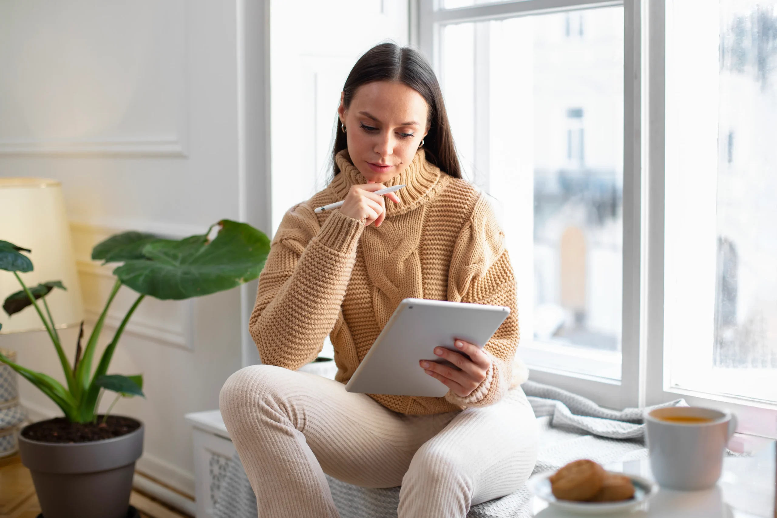 Mujer leyendo un iPad junto a una ventana, explorando artículos del blog sobre bienestar y desarrollo personal