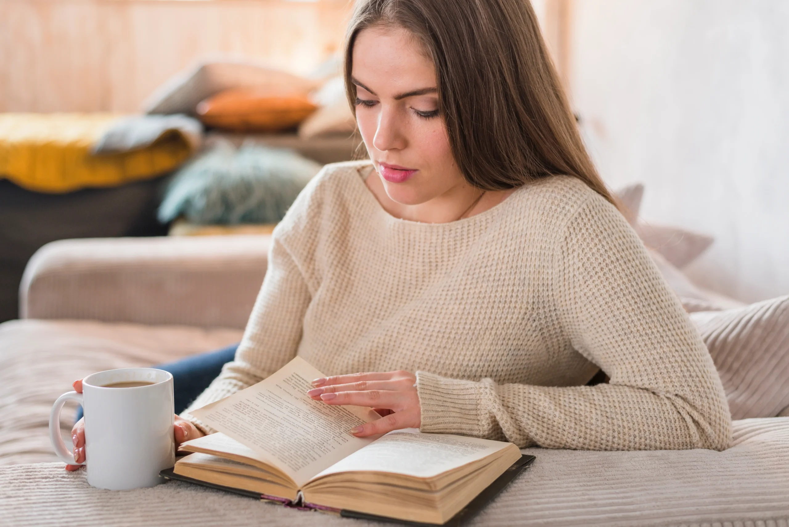 Mujer leyendo un libro en la mesa mientras sostiene una taza de café, disfrutando de la lectura de los libros disponibles en mi colección